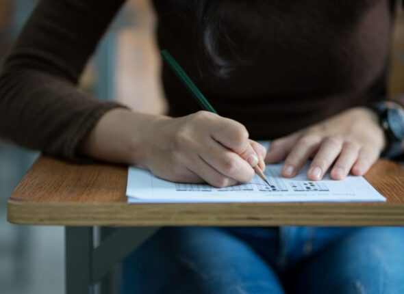 midsection-student-writing-exam-desk-classroom