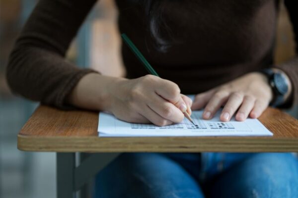 midsection-student-writing-exam-desk-classroom