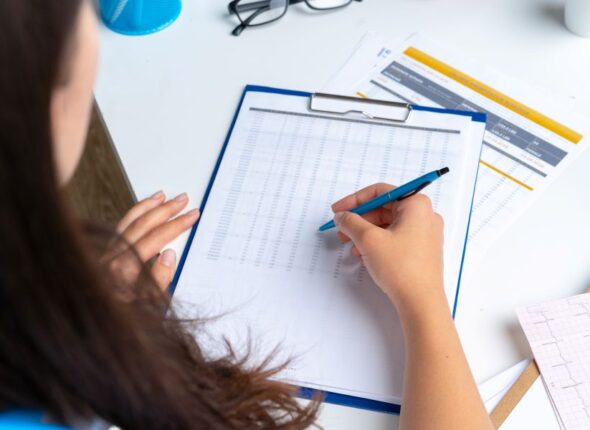 woman-doctor-taking-notes-clipboard-while-sitting-her-table-office